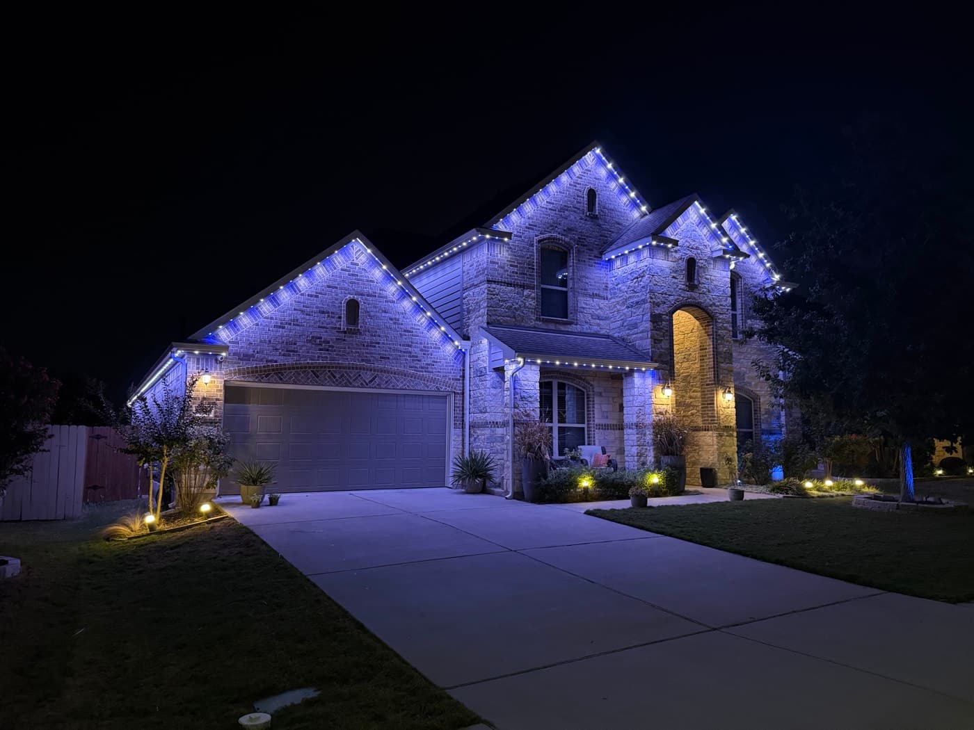 Two-story stone and brick home with blue and white permanent architectural lighting installed by TruLight Chicago